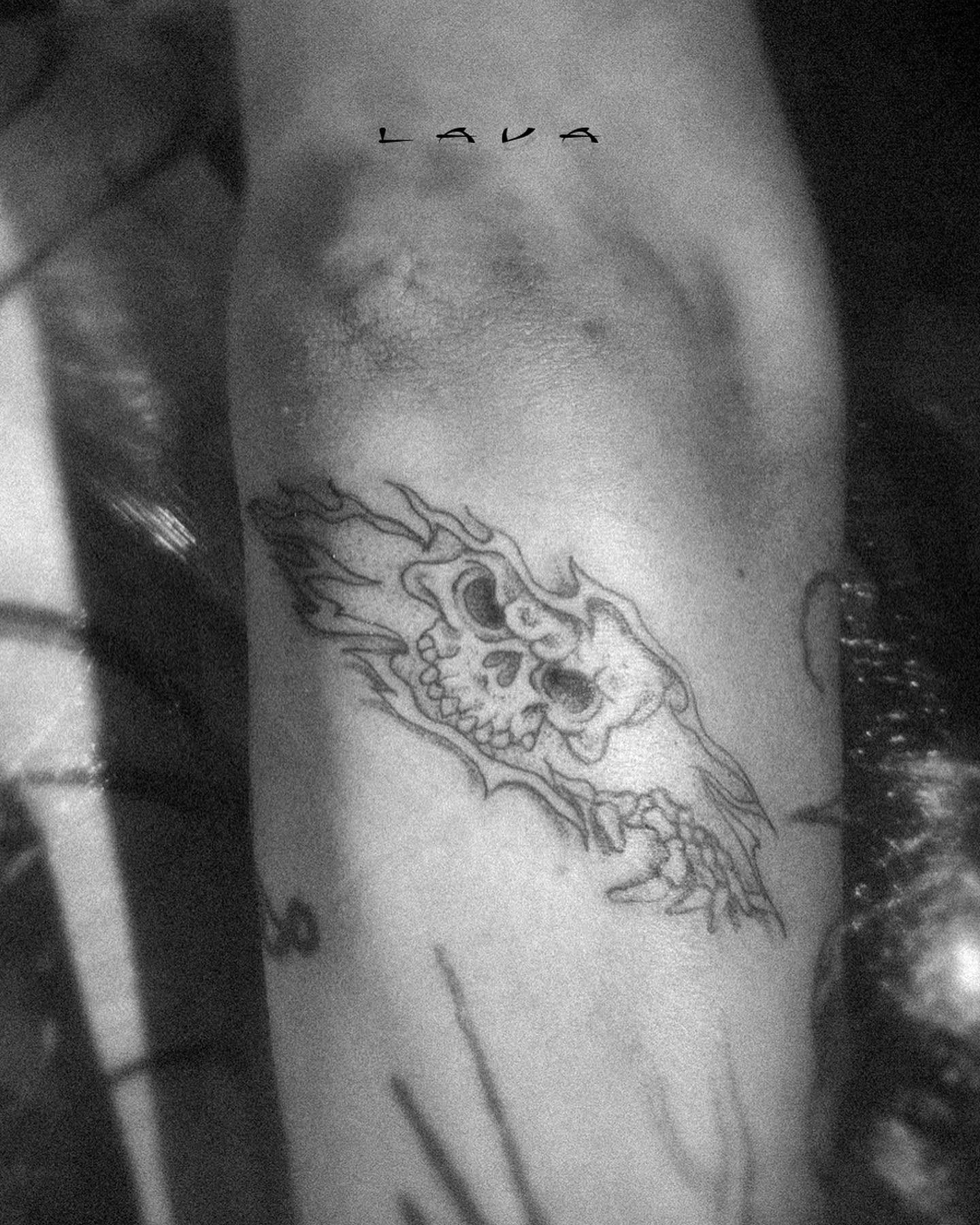 Skull with horizontal flames, blackwork tattoo on arm, high-contrast photograph